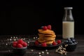 View of plate with stacked pancakes, blueberries, raspberries and bottle of milk, on table and dark background with white flowers