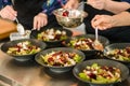 view on plates with salad and hands of people which adds ingredients. Buffet and catering concept Royalty Free Stock Photo