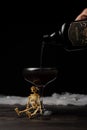 View of poison bottle pouring black Halloween cocktail into glass with skeleton on table with spider web and black background, Royalty Free Stock Photo