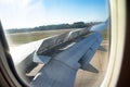 View from the porthole of an airplane wing taking off over the runway at high speed during sunset. The ground passes under the