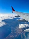 View from the porthole on the wing of an airplane flying above the clouds, mountains are visible below. Royalty Free Stock Photo
