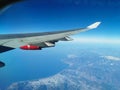 View from the porthole on the wing of an airplane with a red aircraft engine, in the morning over beautiful mountains with snowy Royalty Free Stock Photo