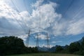 Power lines and pylons in silhouette against a blue sky with white clouds and trees below Royalty Free Stock Photo