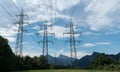 Power lines and pylons in silhouette against a blue sky with white clouds and trees below Royalty Free Stock Photo