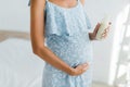 View of pregnant woman in blue dress holding bottle of yoghurt