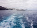 View of Puerto Calero in Lanzarote, Canary Islands, Spain. Picture from a boat going out to sea with the foam wake and the town in Royalty Free Stock Photo