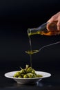 View of pure olive oil pouring on a metal spoon and overflowing into a plate with tempting olives