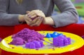 View of purple kinetic sand and forms for modeling on the woman hands molding ball background