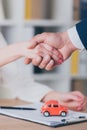 View of realtor shaking hands with customer near house model in office