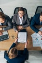 View of recruiter looking at camera near colleagues and employee with resume at table