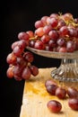 View of red grape bunches in glass stand, on wooden table, with selective focus, black background, Royalty Free Stock Photo