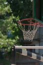 View of red metal basketball hoop with white net and backboard against the green park trees and nearby handball goal Royalty Free Stock Photo