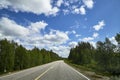 View from relief car windscreen on the blue sky with white clouds, grey asphalt road and landscape with forest and green teeses. Royalty Free Stock Photo