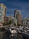 View of residential high-rise buildings on the shore of False Creek in Vancouver downtown with marina and yacht boats in front.