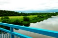 View of river and fields with haystacks, trees and nature over the railing of the old blue bridge Royalty Free Stock Photo