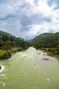 View of a river flowing in a valley surrounded by greenery with clouds over mountains in Bhutan. Royalty Free Stock Photo
