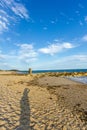 An view of a rocky groyne breakwater with the shadow of the photographer along a sandy beach, choppy blue water and crashing