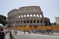 View of the Roman Colosseum. Tourists cross the street and walk to the historic site.