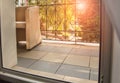 View from the room to the terrace or balcony with a metal railing. The sun shines through a transparent curtain and trees during