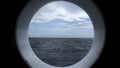 View from round deck window to sea. Clip. Beautiful seascape with mountain coast on horizon from round window. Sea Royalty Free Stock Photo