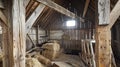 A view of a rustic barn loft with old hay bales and farming equipment stored inside. Cracks in the wooden beams reveal Royalty Free Stock Photo