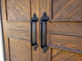 Angled view of rustic, wooden doors with black iron handles on a light colored building Royalty Free Stock Photo