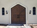 Front view of rustic, wooden doors with black iron handles on a light colored building Royalty Free Stock Photo