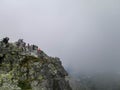 View of Rysy peak in Slovakia with tourists taking a break at the top of the mountains. With moody cloudy sky. Barely visible