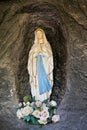 View of Saint Mary statue praying in a stone cave with flowers at her feet