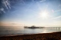 View from sand beach to water of sea, waves and pier in a nice day or evening with blues sky, bright sun and white clouds. The Royalty Free Stock Photo