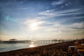 View from sand beach to water of sea, waves and pier in a nice day or evening with blues sky, bright sun and white clouds. The Royalty Free Stock Photo