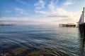 View from sand beach to water of sea, waves and pier in a nice day or evening with blues sky, bright sun and white clouds. The Royalty Free Stock Photo