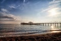 View from sand beach to water of sea, waves and pier in a nice day or evening with blues sky, bright sun and white clouds. The Royalty Free Stock Photo