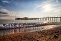 View from sand beach to water of sea, waves and pier in a nice day or evening with blues sky, bright sun and white clouds. The Royalty Free Stock Photo