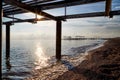 View from sand beach to water of sea, waves and pier in a nice day or evening with blues sky, bright sun and white clouds. The Royalty Free Stock Photo