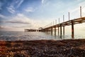 View from sand beach to water of sea, waves and pier in a nice day or evening with blues sky, bright sun and white clouds. The Royalty Free Stock Photo