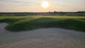 View of a sand bunker on a golf course, with green turf and the setting sun in the background. Royalty Free Stock Photo