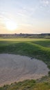 View of a sand bunker on a golf course, with green turf and the setting sun in the background. Royalty Free Stock Photo