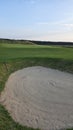 View of a sand bunker on a golf course, with green turf and the setting sun in the background. Royalty Free Stock Photo