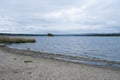 View of the sandy beach and lake on a cloudy day. Spring river landscape. Boundless beautiful sky, a blue lake with a small green Royalty Free Stock Photo