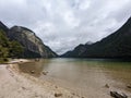 View from the sandy shore of lake Konigssee surrounded by rocky Alps under cloudy sky