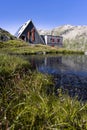 View of the Scaletta hut near the Greina Pass in Blenio, Switzerland. In the foreground is a pond reflecting the hut and
