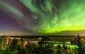 View from scandinavian hill to bright green aurora lights almost on the whole sky over tree tops in Sweden, river, clear skies Royalty Free Stock Photo