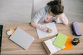 View of schoolchild doing homework while sitting at wooden desk near book, notebooks, laptop and pencil case