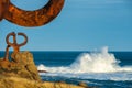 View of a sculpture of the Peine del Viento, with waves in the background, a sunny winter day