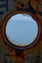 View of sea through the round window of an old, rusted ships hull