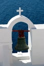 View of sea surface through traditional Greek white church arch with cross and bells in Oia village of Cyclades Island, Santorini, Royalty Free Stock Photo