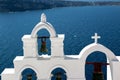 View of sea surface through traditional Greek white church arch with cross and bells in Oia village of Cyclades Island