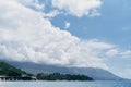 View from the sea to a green island with mountains, trees and houses against a blue sky with white clouds Royalty Free Stock Photo