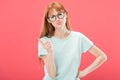 View of serious redhead woman in glasses and t-shirt standing with hand on hip and shaking finger isolated on pink